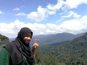 Portrait of smiling young woman standing against mountains