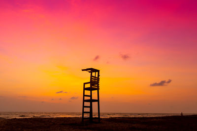 Silhouette cross on beach against sky during sunset