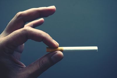 Cropped hand holding cigarette against gray background