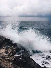 Waves splashing on rocks at shore against sky