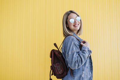 Young woman standing against yellow wall