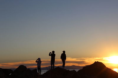 Silhouette people standing on rock against sky during sunset