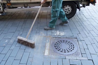 Low section of street sweeper sweeping by manhole on footpath