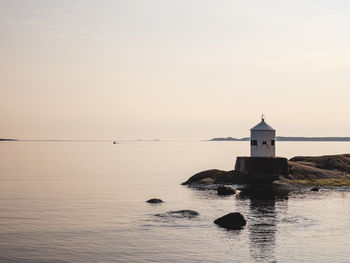 Lighthouse by sea against sky during sunset