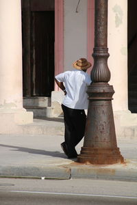 Rear view full length of man standing by pole on sidewalk