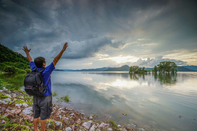 Rear view of man standing by lake against sky