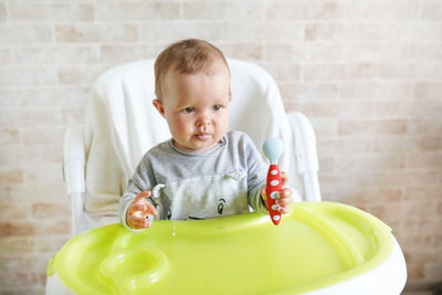 Cute baby girl holding spoon on high chair at home