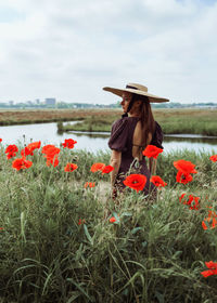 Rear view of woman standing amidst plants on field against sky