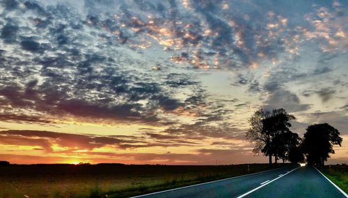 Road by silhouette trees against sky during sunset