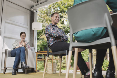 Businesswoman using smart phone while colleagues sitting on chairs in portable office truck