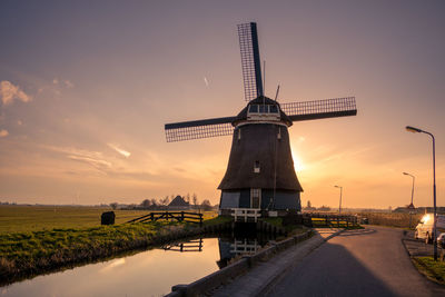 Traditional windmill by road against sky during sunset