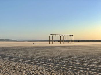 Swingset on beach against clear sky during sunset