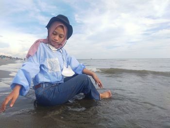 Young woman sitting on beach against sky