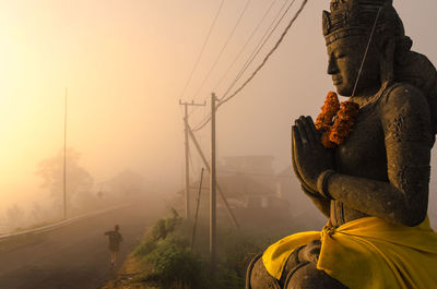 Female sculpture by road against sky during foggy weather