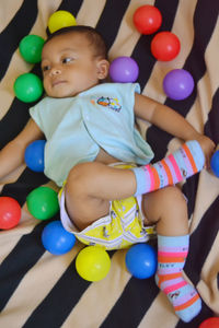 Cute boy lying amidst balls on bed at home