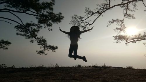 Silhouette man jumping on field against sky during sunset