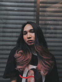 Portrait of young woman standing against wall