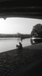 People sitting on riverbank against sky