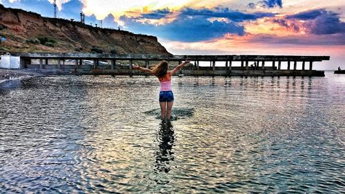 Rear view of boy standing at sea shore against sky