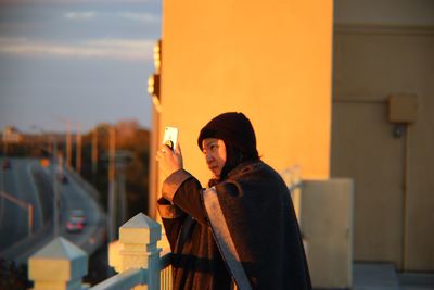 Woman photographing from mobile phone while standing in balcony