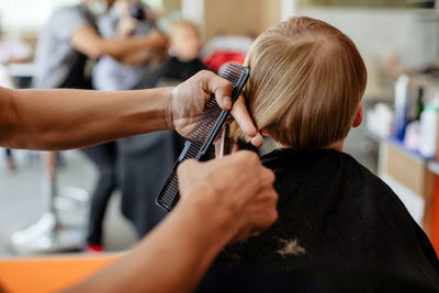 Crop barber doing haircut to little boy