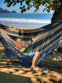 Cute girl writing on book while sitting on hammock at beach