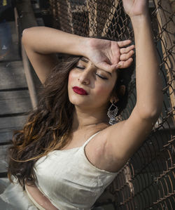 Close-up of beautiful woman with eyes closed sitting by chainlink fence