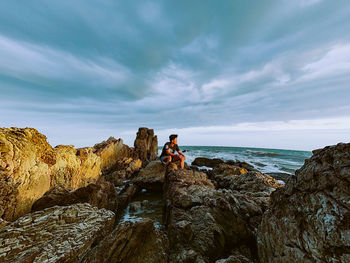 People sitting on rock by sea against sky