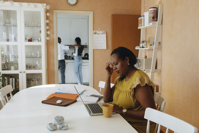 Female freelancer with head in hand using laptop while sitting at table