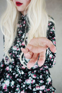 Midsection of woman gesturing while standing against wall