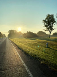 Road amidst field against sky during sunset