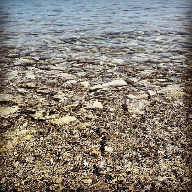 water, beach, shore, high angle view, tranquility, sea, nature, pebble, sand, stone - object, day, outdoors, tranquil scene, beauty in nature, no people, rock - object, textured, sunlight, rippled, abundance