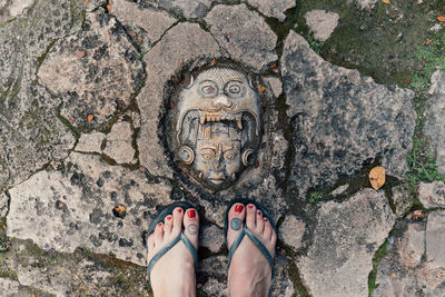 Mayan fce engraved in stone on the ground with toes in flip flops