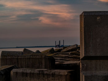 Wooden posts on pier by sea against sky during sunset