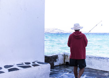 Rear view of man standing by sea against clear sky