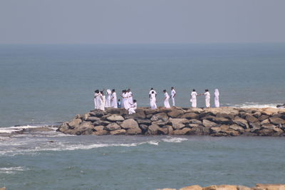 Group of people on rocks by sea against clear sky
