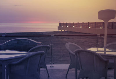 Empty chairs by swimming pool against sky during sunset