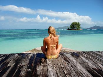 Rear view of young woman sitting on pier by sea against sky