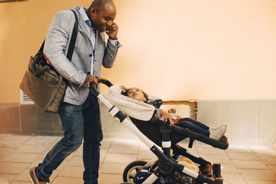 Smiling father talking on mobile phone while pushing daughter in carriage on footpath