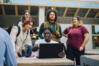 Happy male and female friends studying online through laptop in university campus