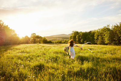 Rear view of woman walking on field against sky during sunset