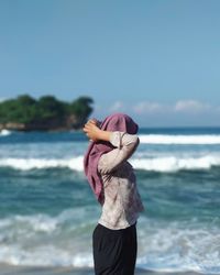 Side view of woman standing at beach against sky