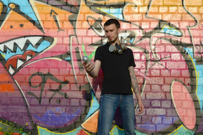 Full length of young man standing against graffiti wall