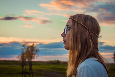 Portrait of young woman looking away against sky during sunset