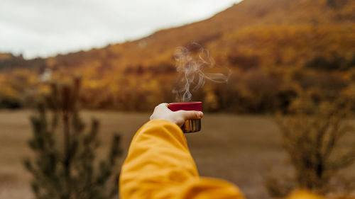 A young man in a yellow jacket pours and drinks tea from a thermos