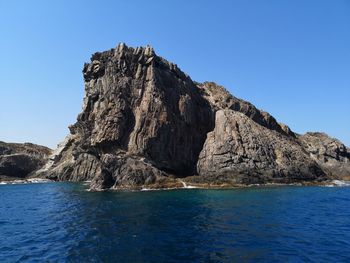 Rock formations by sea against clear blue sky