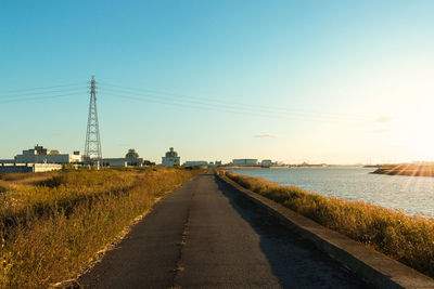 Road by electricity pylon against sky