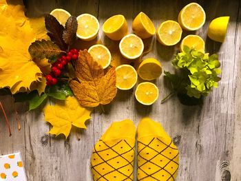 Low section of person standing by lemons and autumn leaves on table