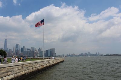 Flag by buildings in city against cloudy sky