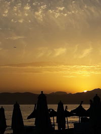 Silhouette parasols at beach against orange sky